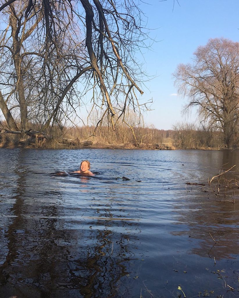 early spring woman swimming in river under a big tree